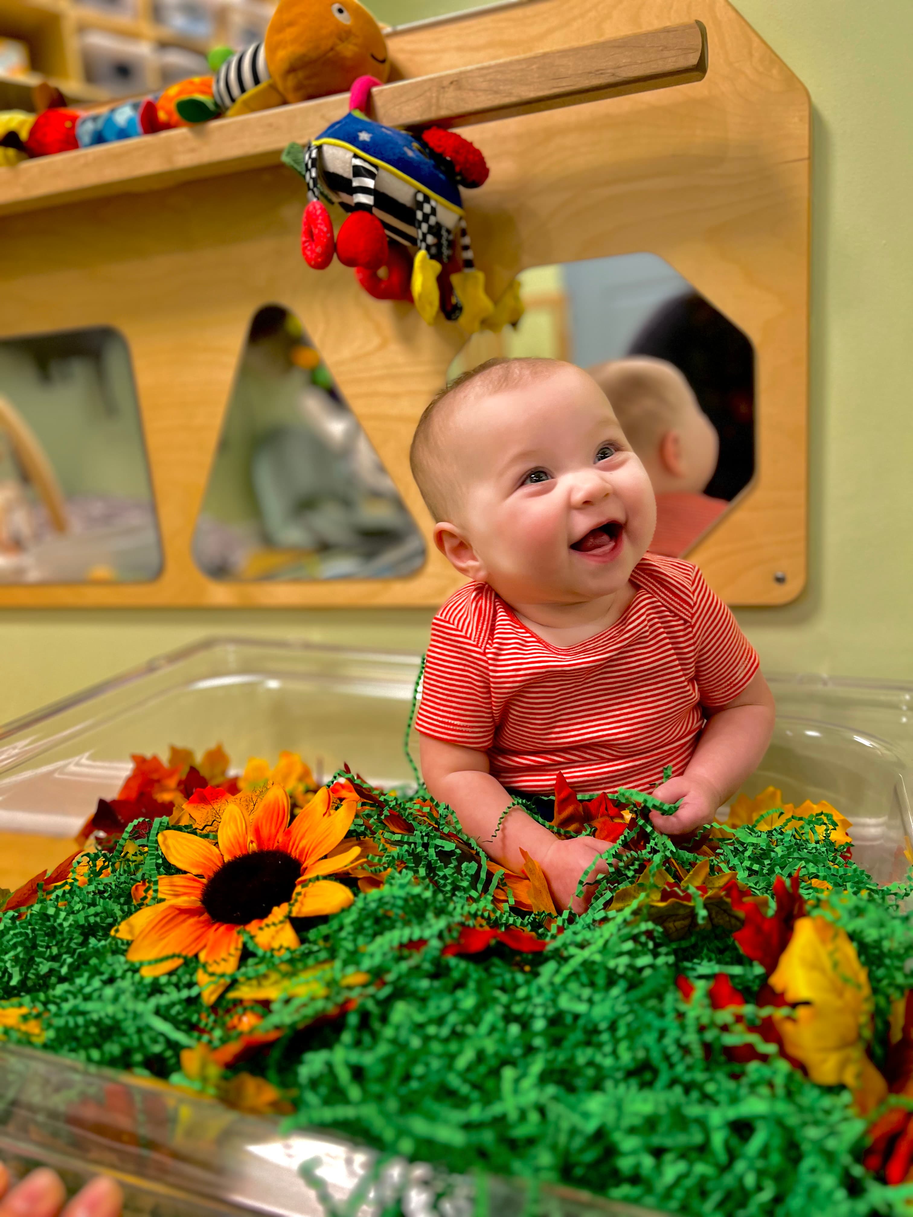 Smiling baby enjoying a fall-themed sensory play bin in a Kinder Prep classroom