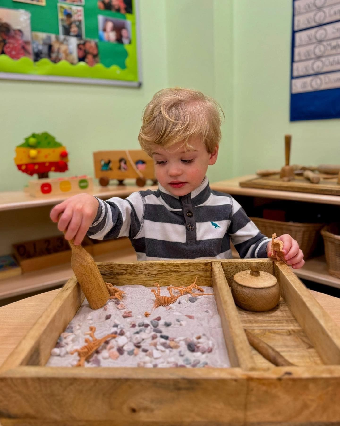 Young child exploring a Montessori sensory tray with dinosaur figures at Kinder Prep