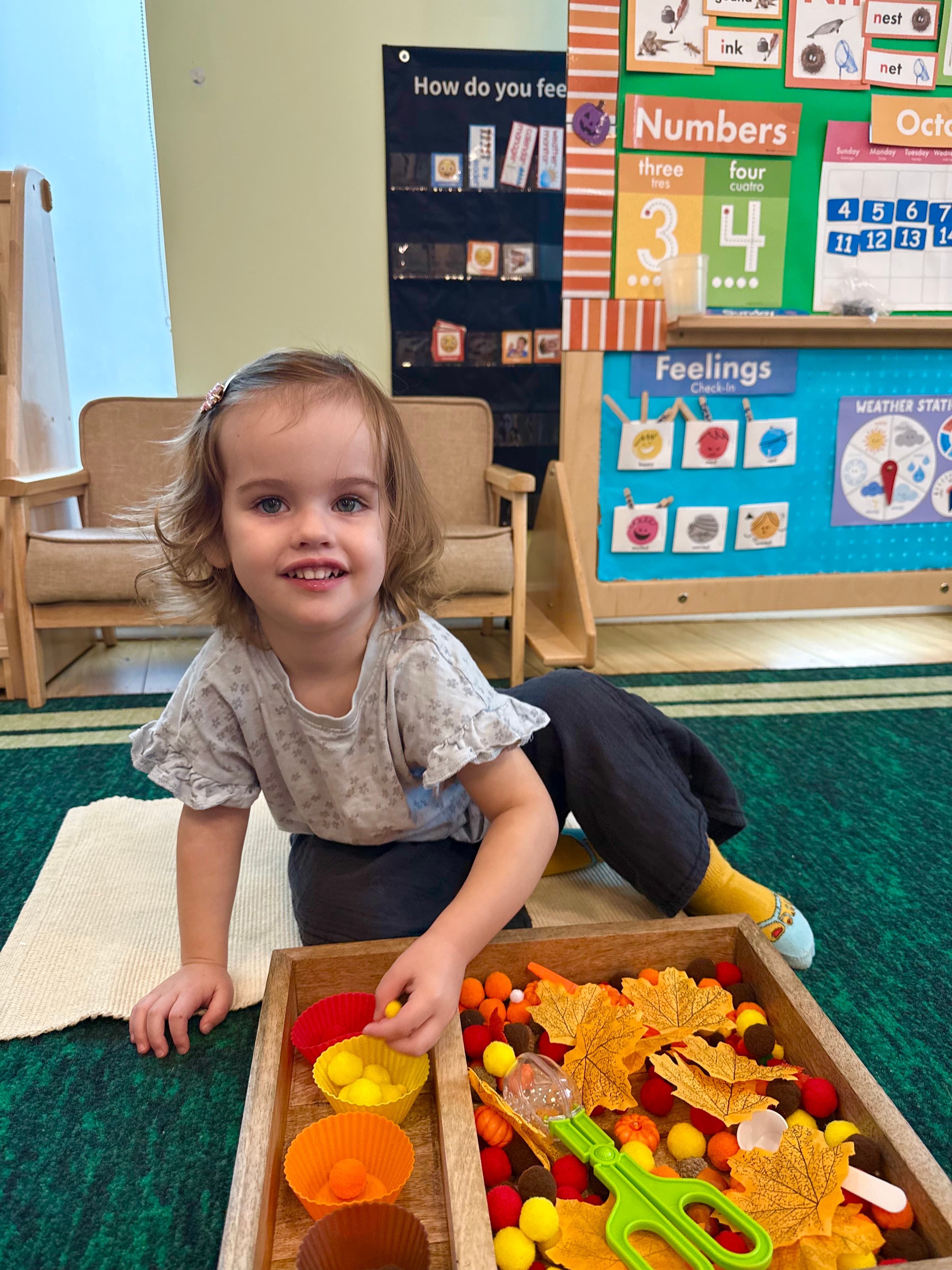 Child exploring a fall sensory activity with leaves and pom-poms