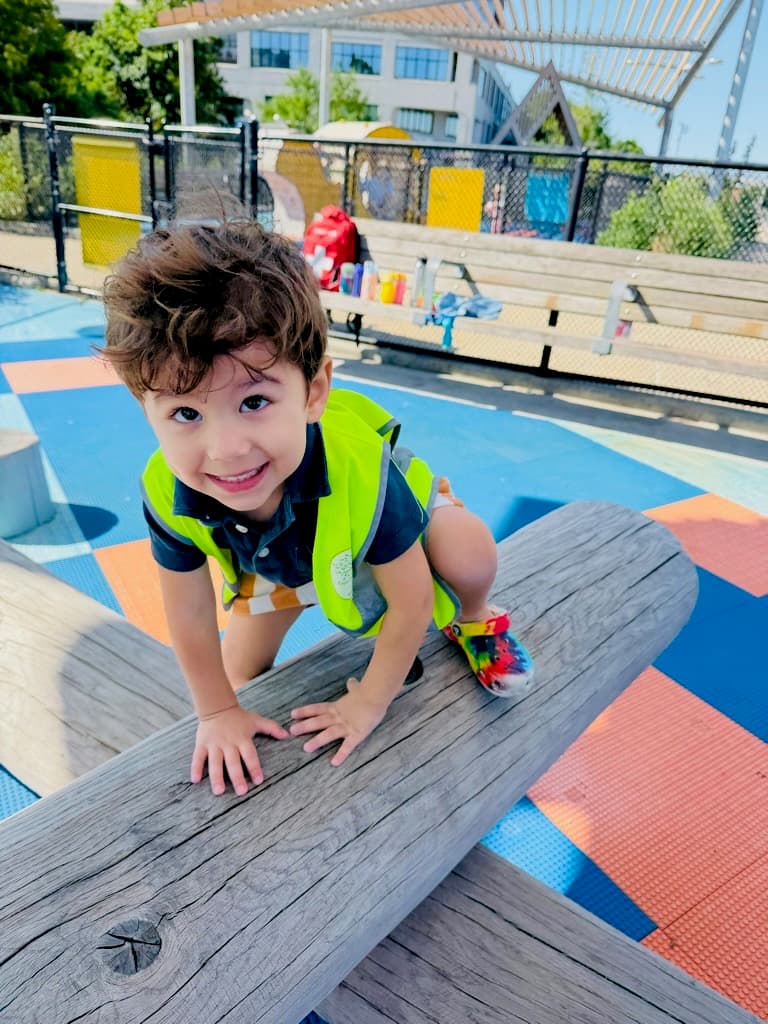 Smiling Pre-K child climbing a wooden play structure at a Brooklyn playground