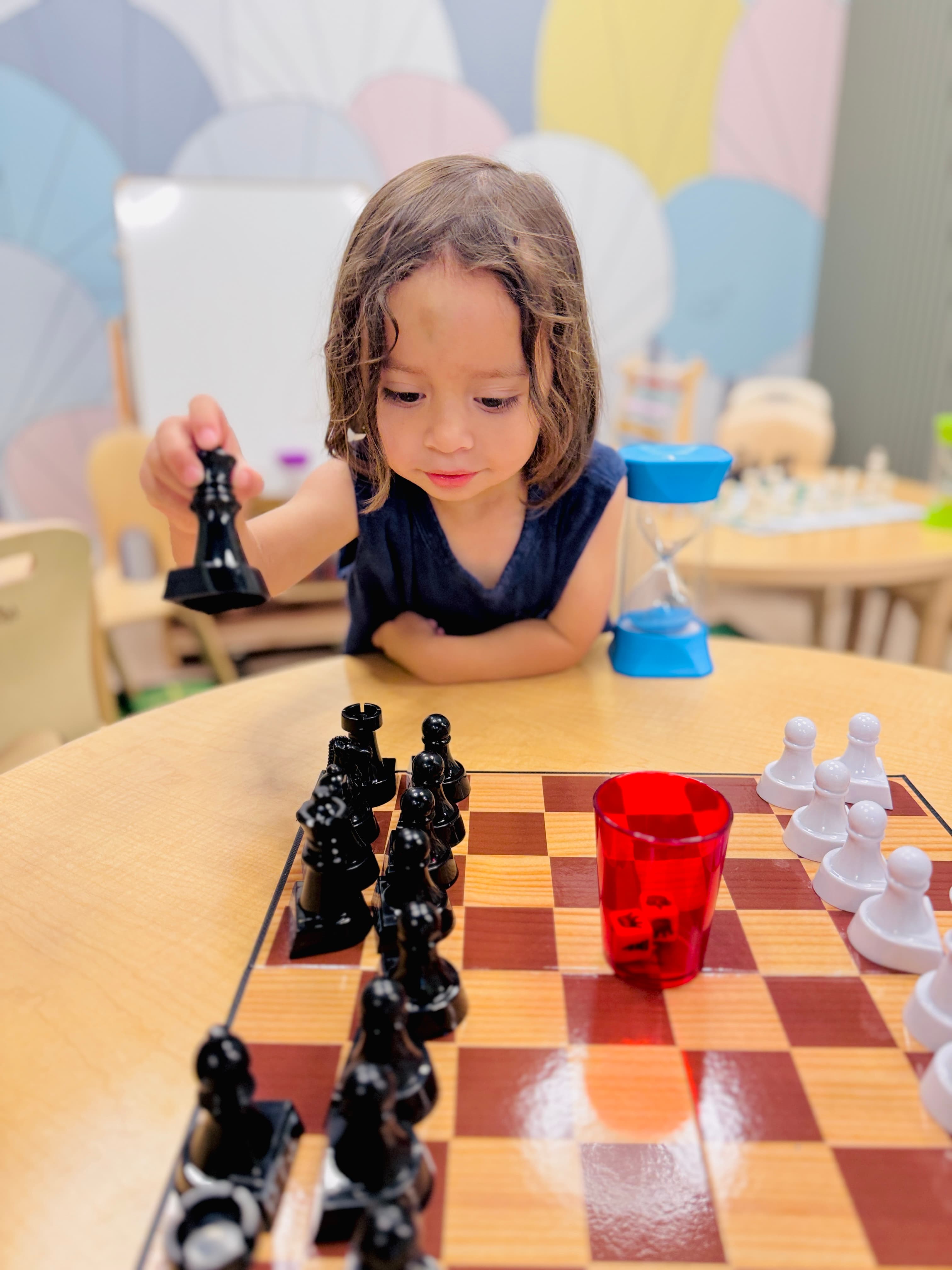Pre-K child concentrating on a move during a chess enrichment class with a sand timer