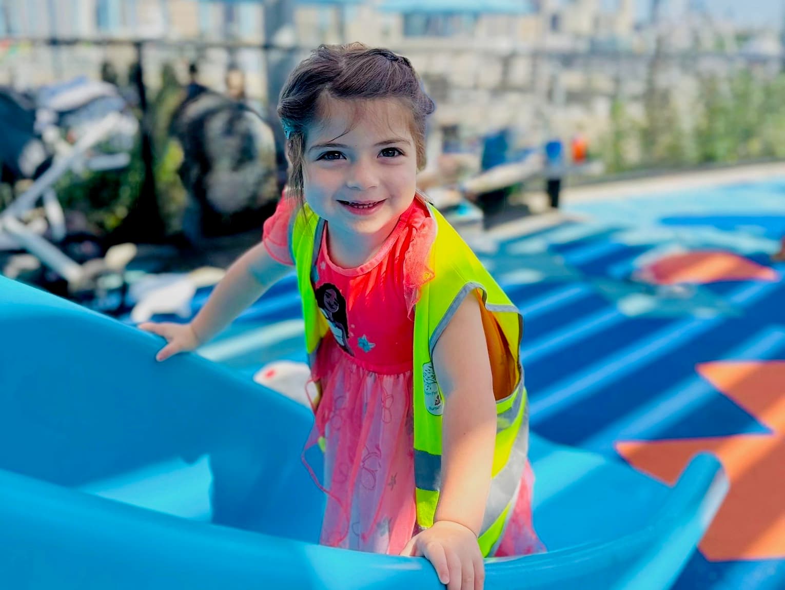 Pre-K child in a safety vest climbing a slide during outdoor play on the rooftop playground