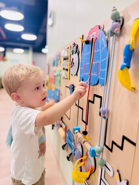Toddler at a sensory wall exploring textures and colors at Kinder Prep