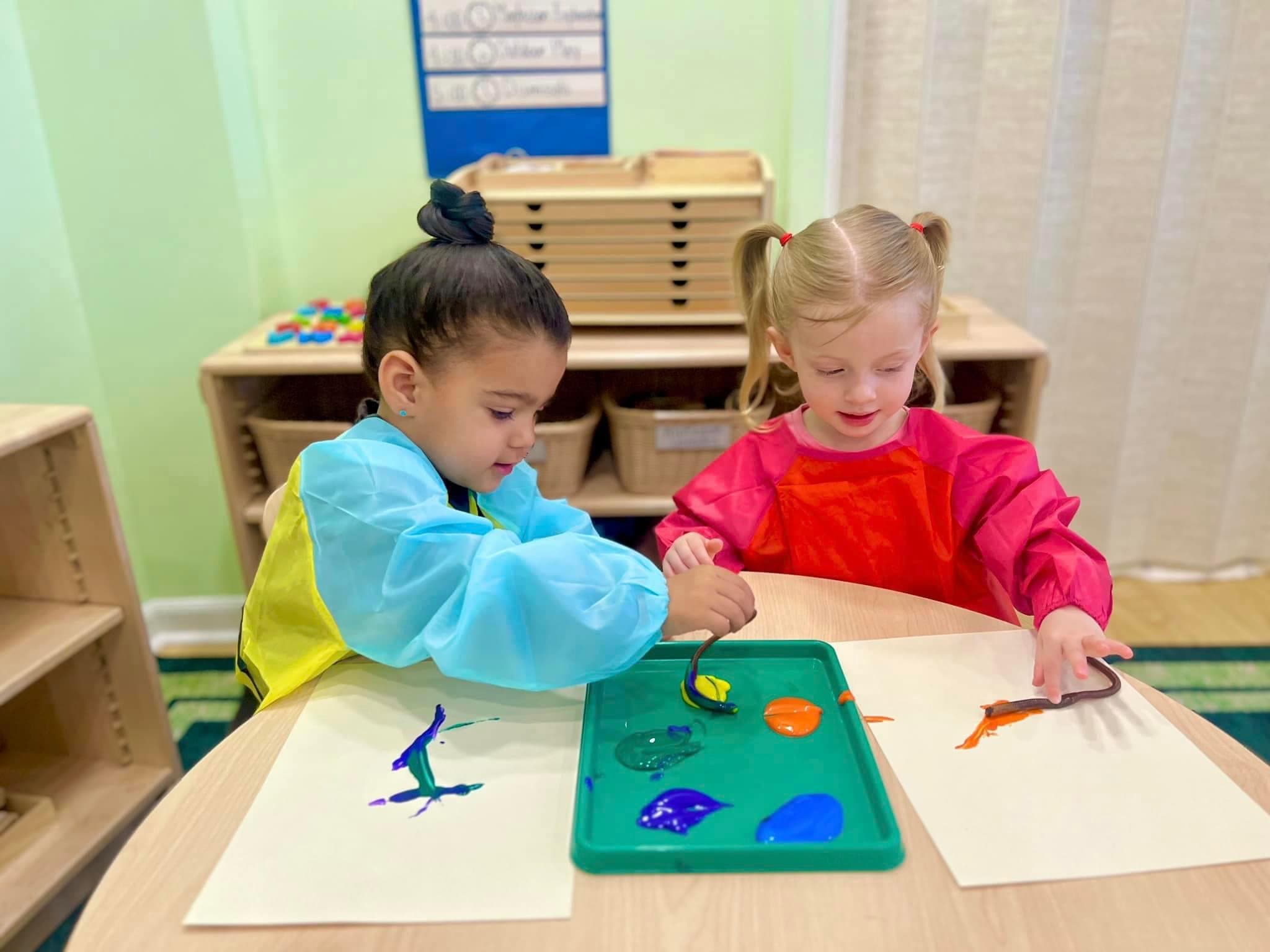 Two early preschoolers in smocks finger painting at Kinder Prep