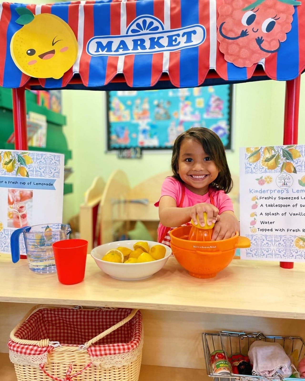 Early preschooler squeezing lemons at the pretend market stand