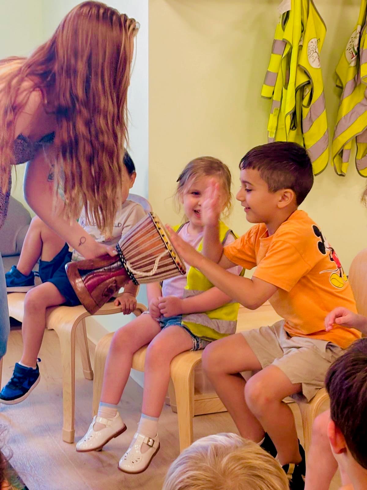 Children clapping and drumming in a hands-on music enrichment class with a specialist at summer camp