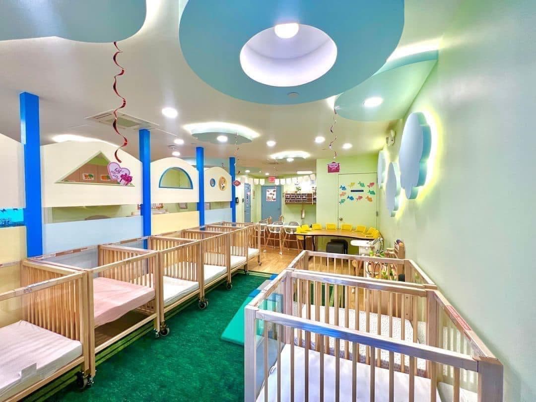 Infant classroom with wooden cribs, play pens, and soft natural light