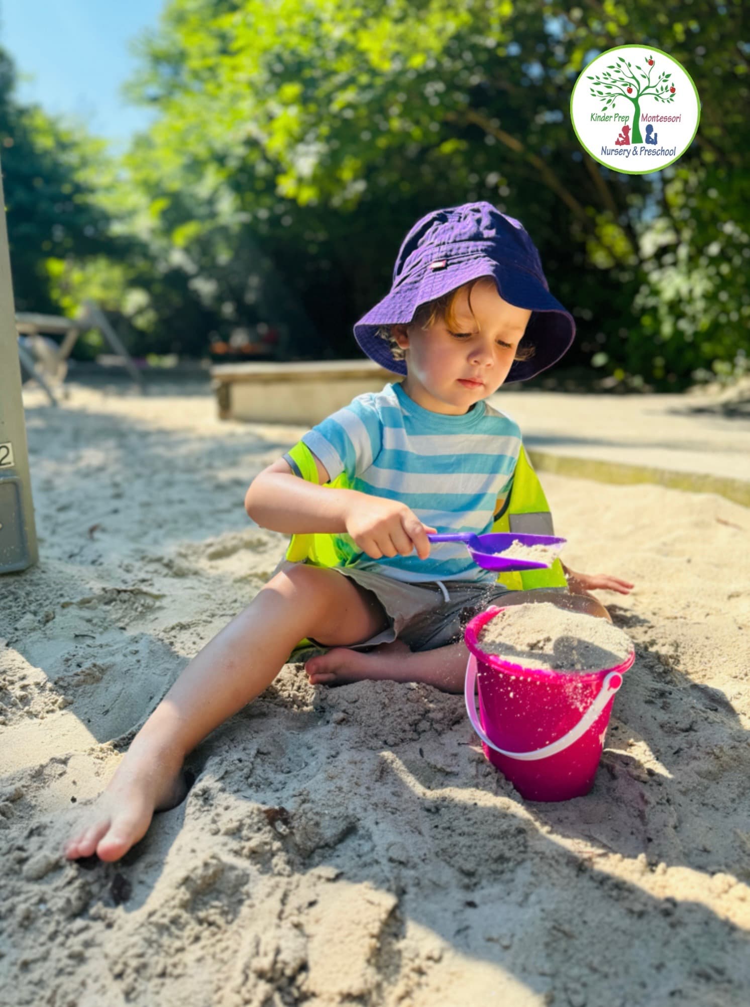 Kinder Prep camper scooping sand into a bucket in the sunny sand pit at Brooklyn Bridge Park