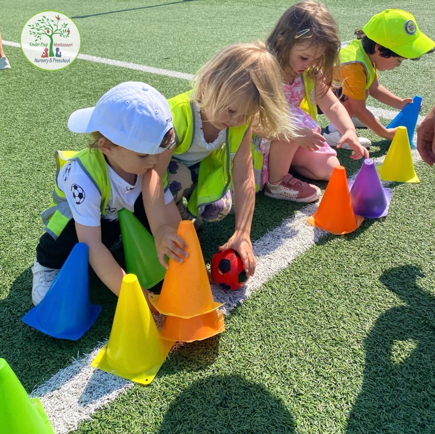 Kinder Prep campers setting up colorful cones on a sunny turf field during a summer sports session